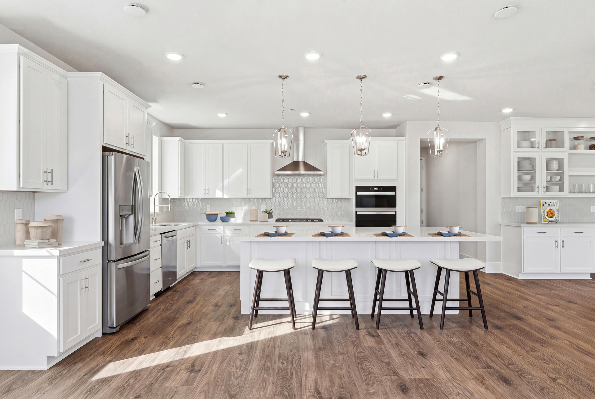 kitchen with white cabinets & counters, wood floors, three brushed nickel pendant lights above island with four espresso barstools