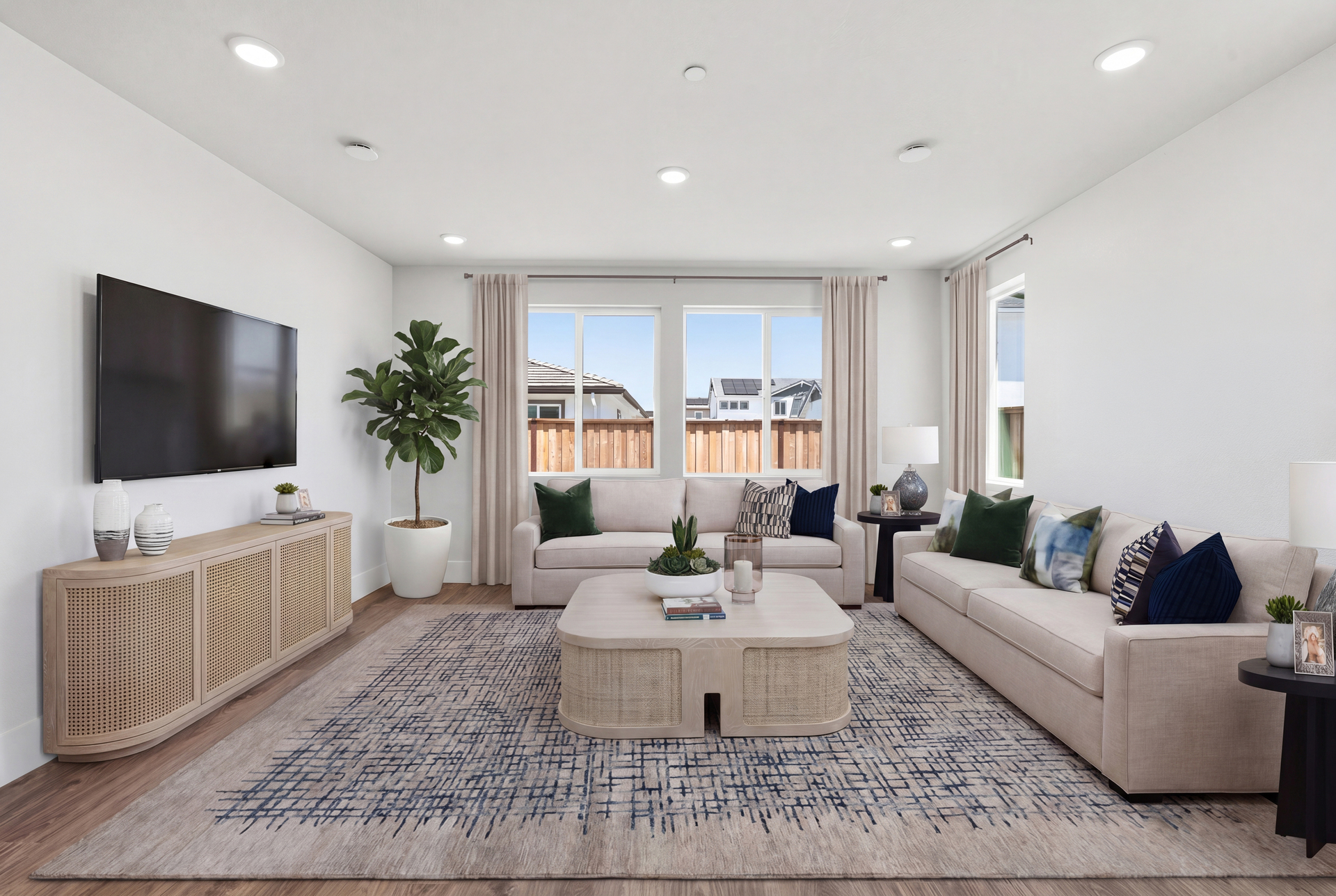 great room with two tans sofas, patterned tan & blue area rug, light wood coffee table, and multiple windows