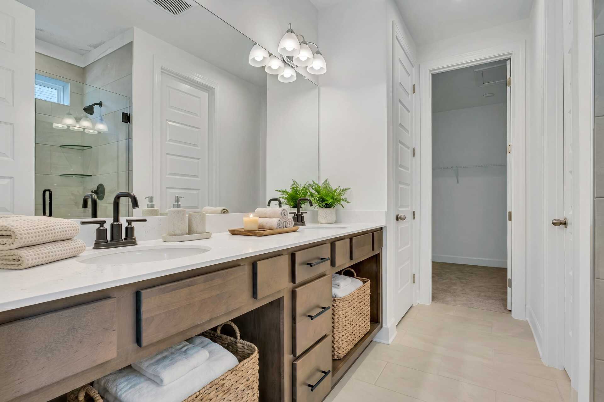 primary bathroom with double sink vanity, wood cabinets, tile flooring, and a glass shower