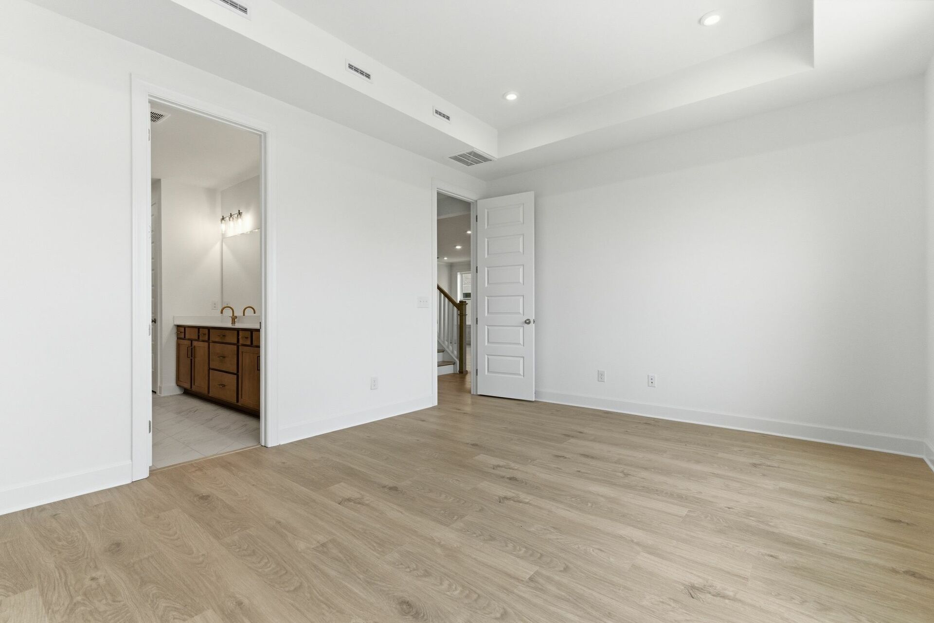 primary bedroom with hardwood floors, large windows, double door walk-in closet, and attached bathroom 