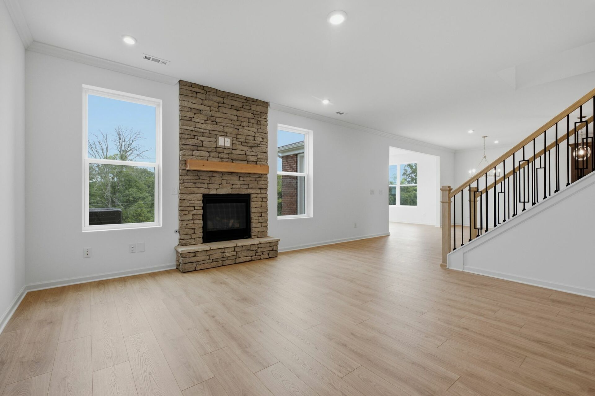 great room with stone fireplace, wood floors, and oak tread stairs with iron railing
