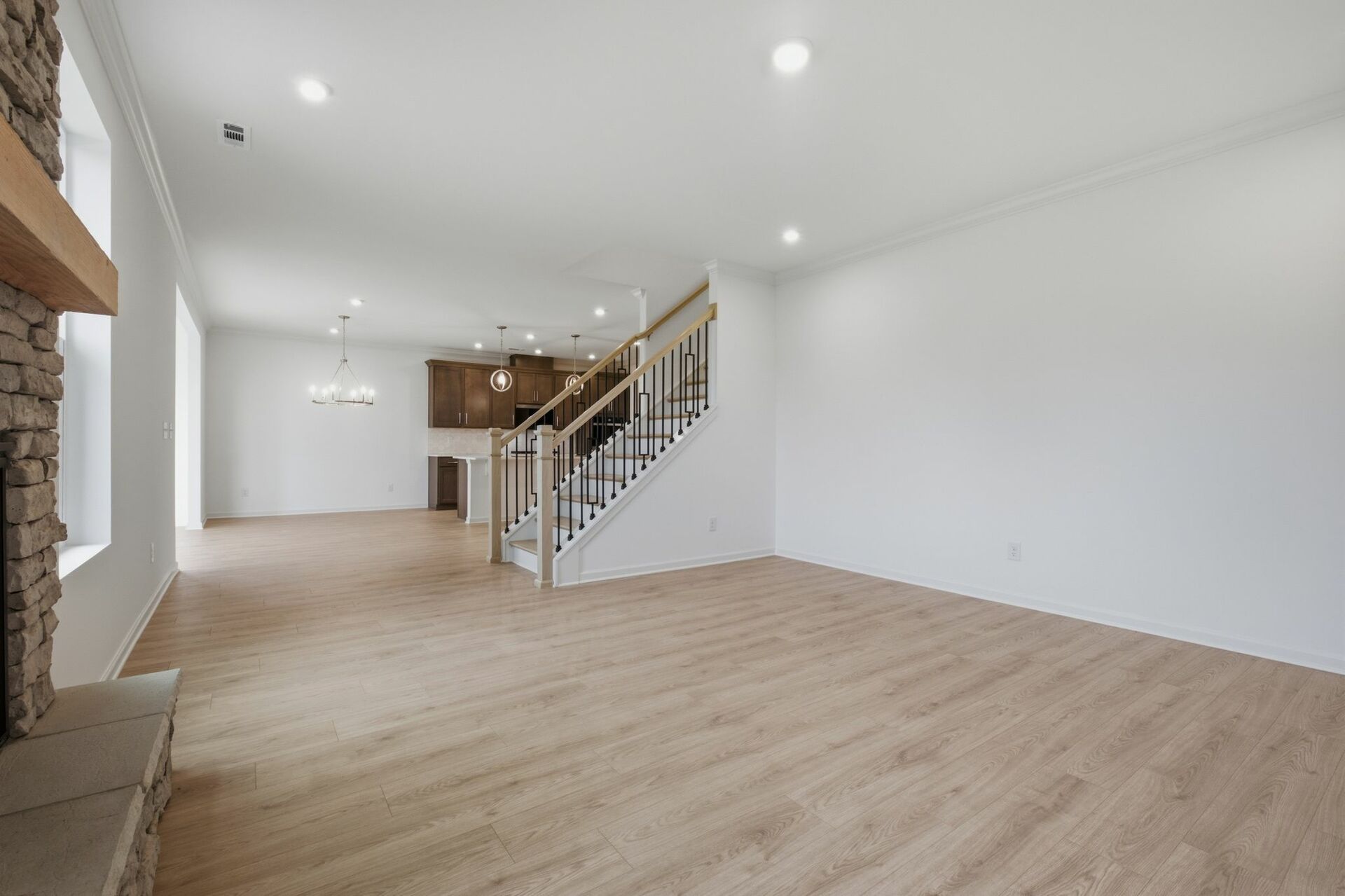 great room with stone fireplace, wood floors, and oak tread stairs with iron railing
