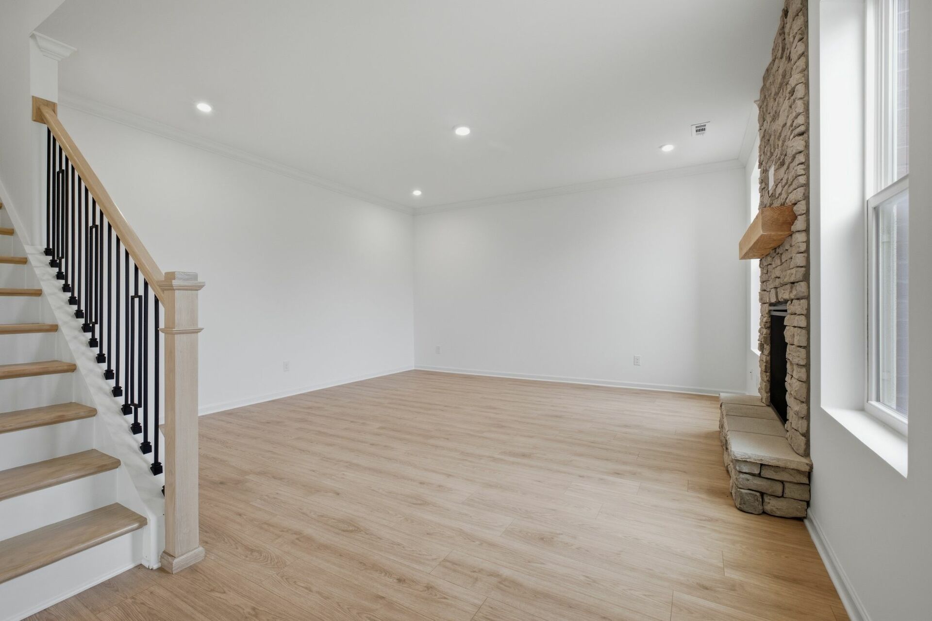 great room with stone fireplace, wood floors, and oak tread stairs with iron railing