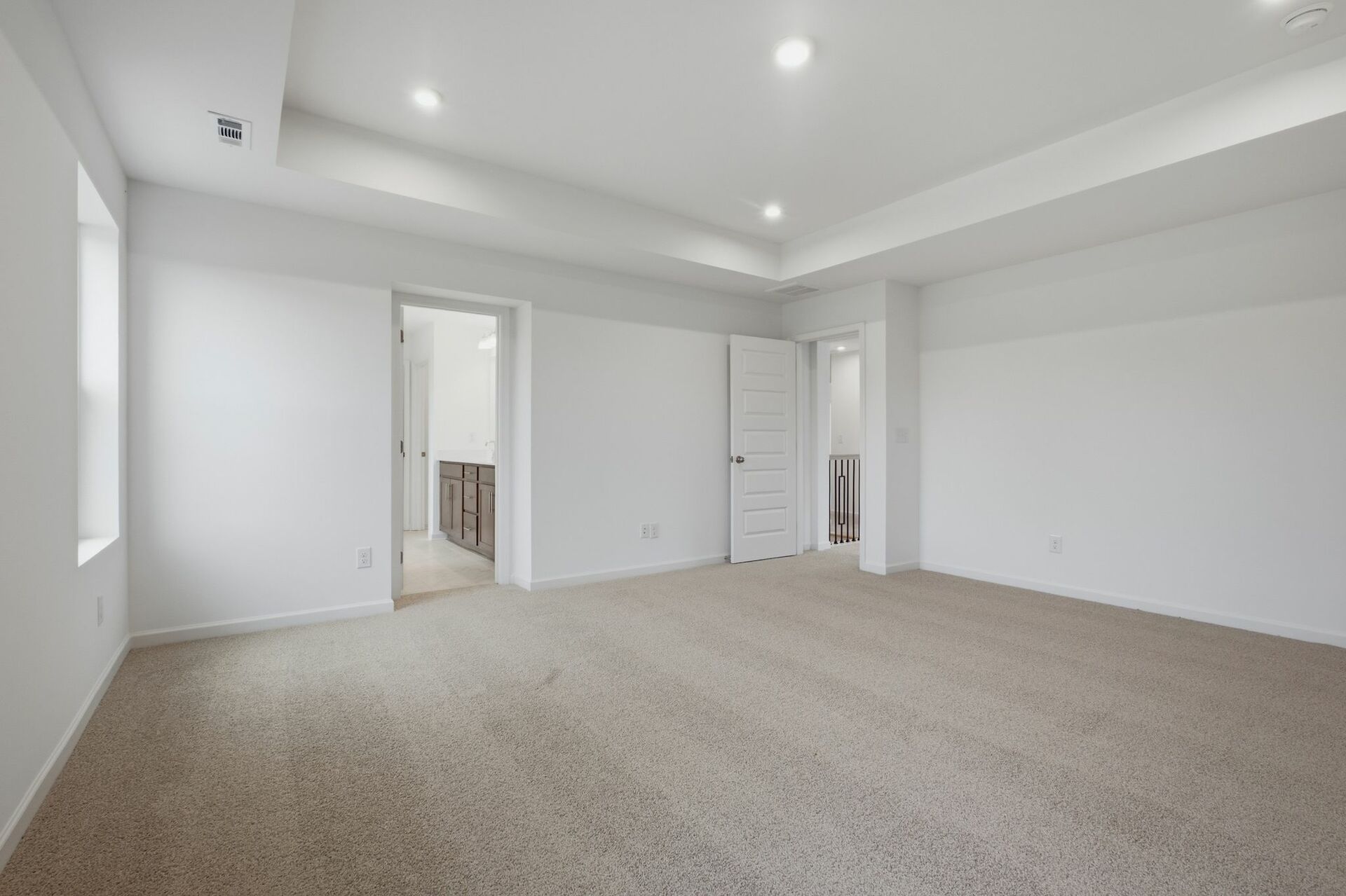 primary bedroom with carpet, large windows, tray ceiling, walk-in closet, and attached bathroom