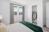 bedroom with a spacious white bed, royal green duvet, and beige rug