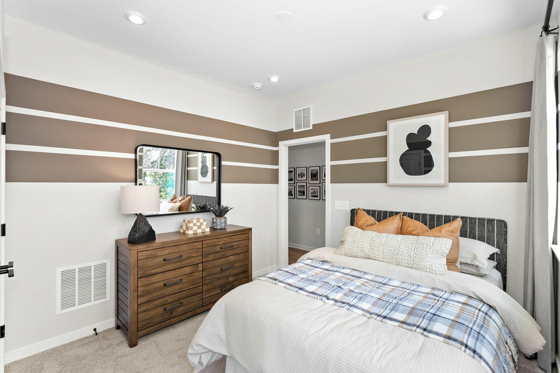 bedroom with large bed, wooden dresser, paintings and mirror