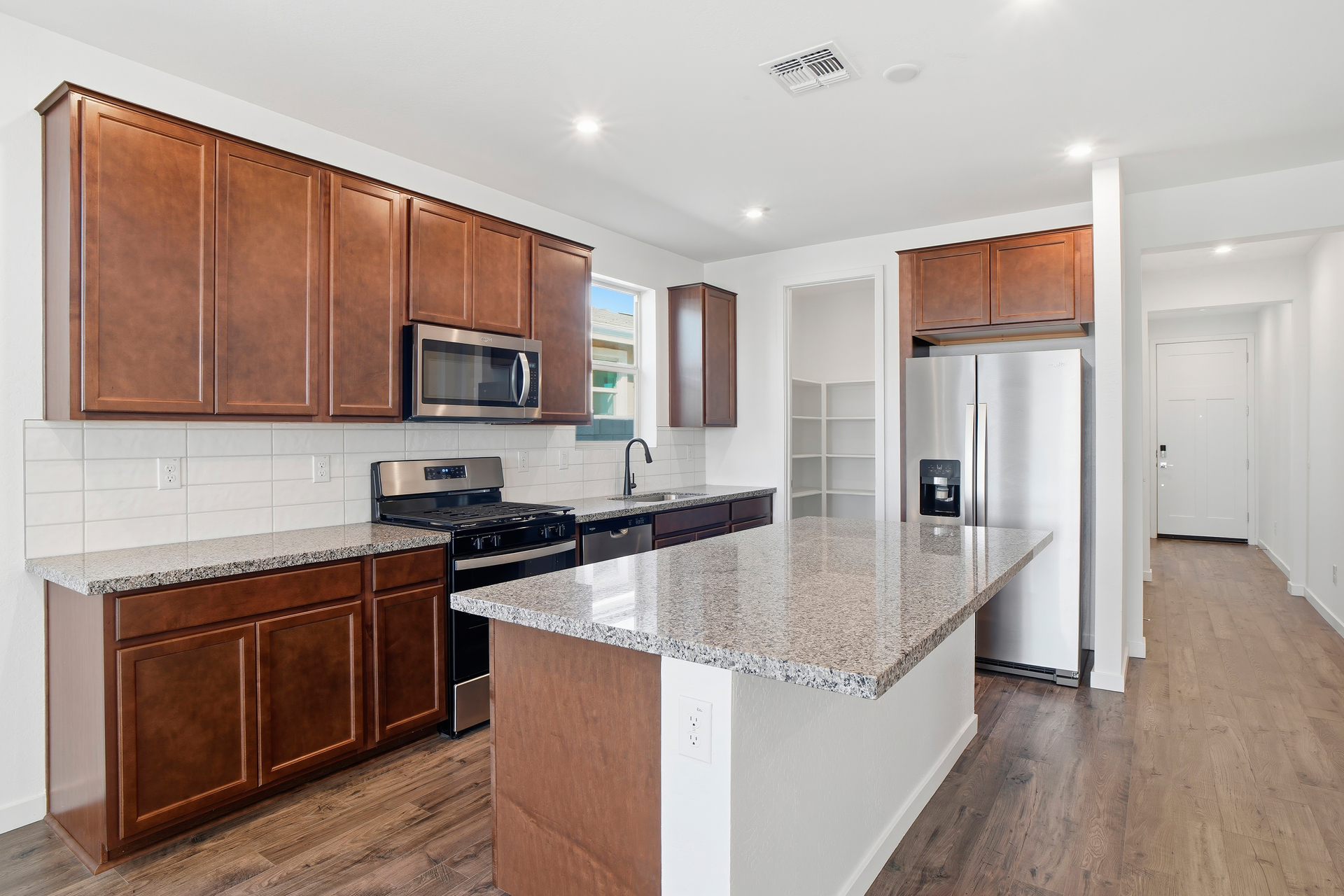 kitchen with brown cabinets, new caledonia countertops, and stainless-steel appliances.