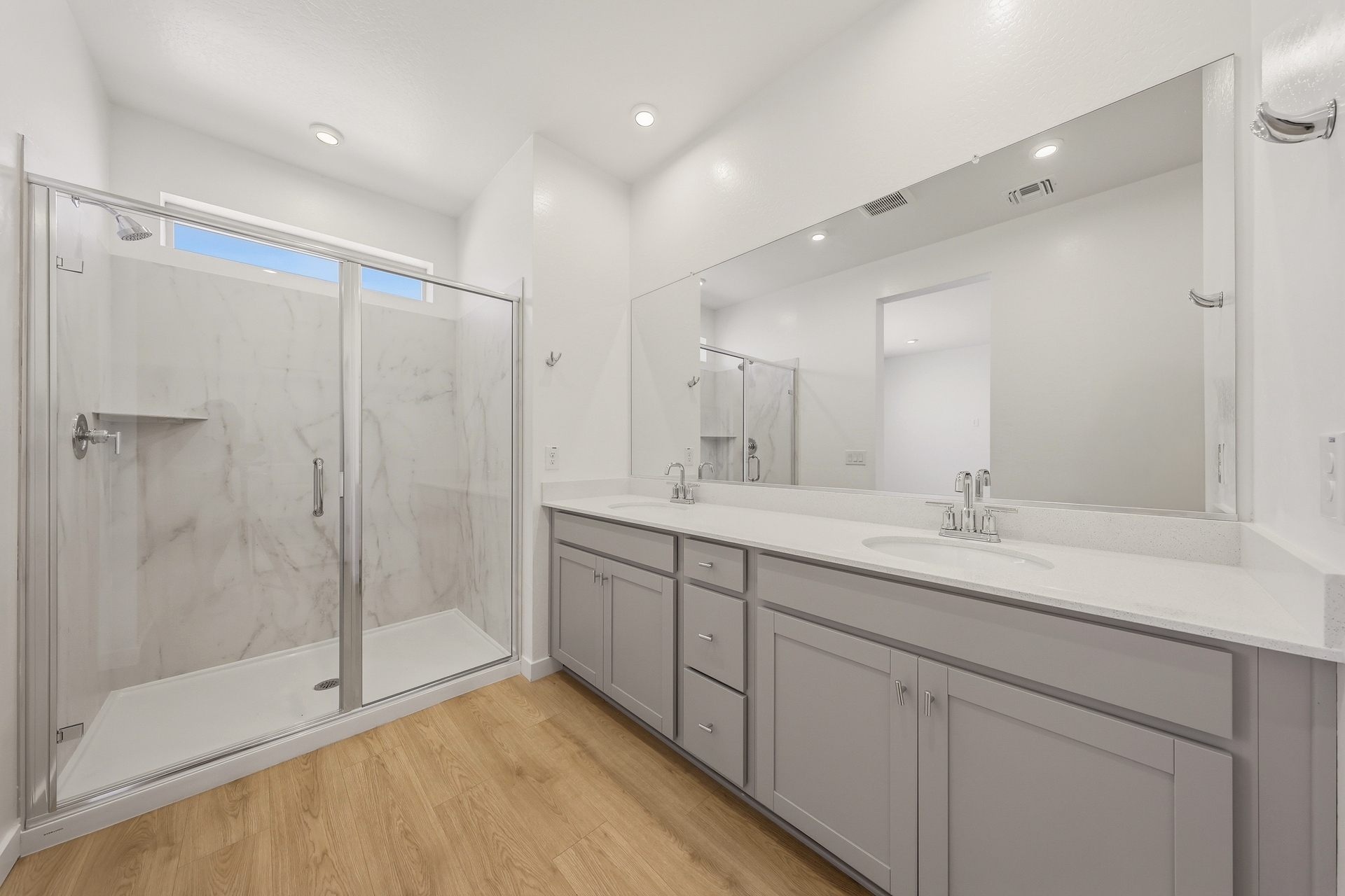 spacious bathroom with large walk-in shower, grey cabinets, and double sink with chrome faucets