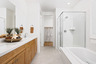 bathroom with light wood cabinets, white counters, tan tile floors, walk-in shower, and separate tub