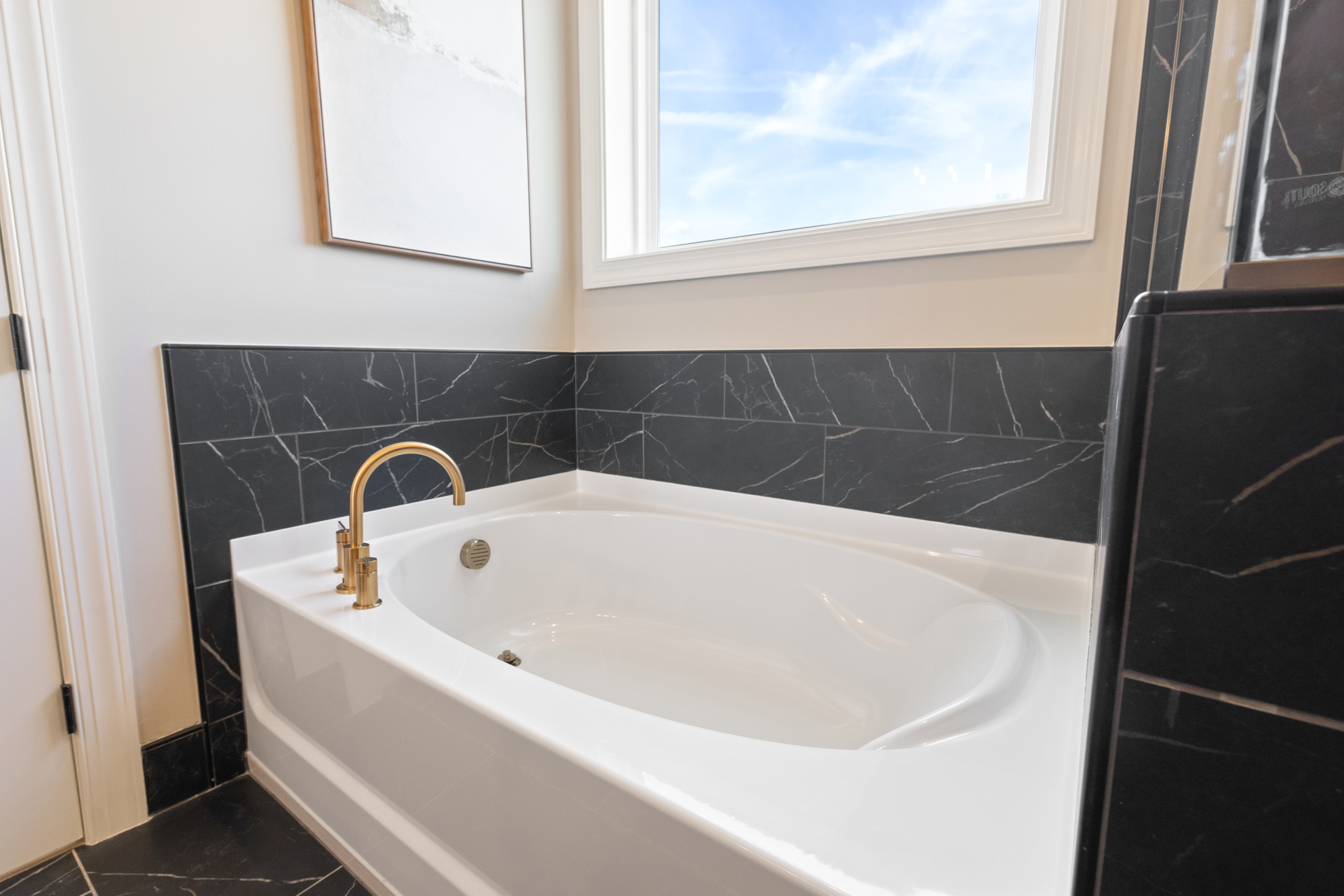 primary bathroom with black mosaic tile, wood cabinets, and gold hardware