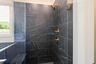 primary bathroom with black mosaic tile, wood cabinets, and gold hardware