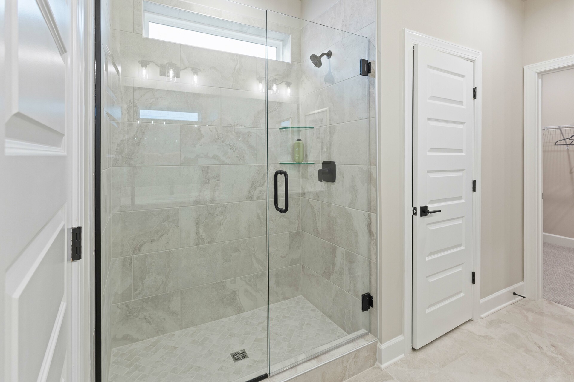 primary bathroom with double sink vanity, wood cabinet, white countertops, and glass walk-in shower