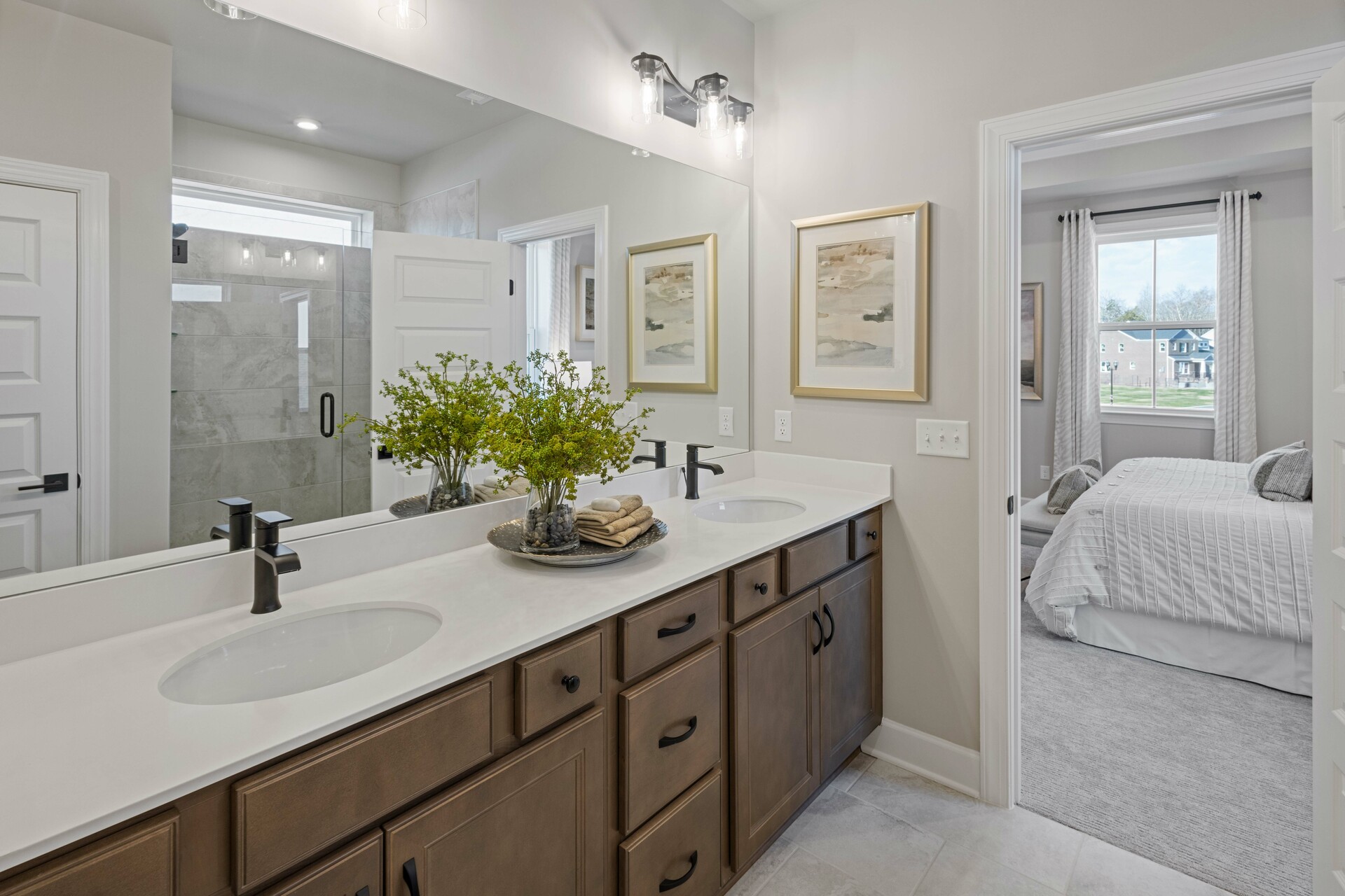 primary bathroom with double sink vanity, wood cabinets, white countertops, and a glass walk-in shower
