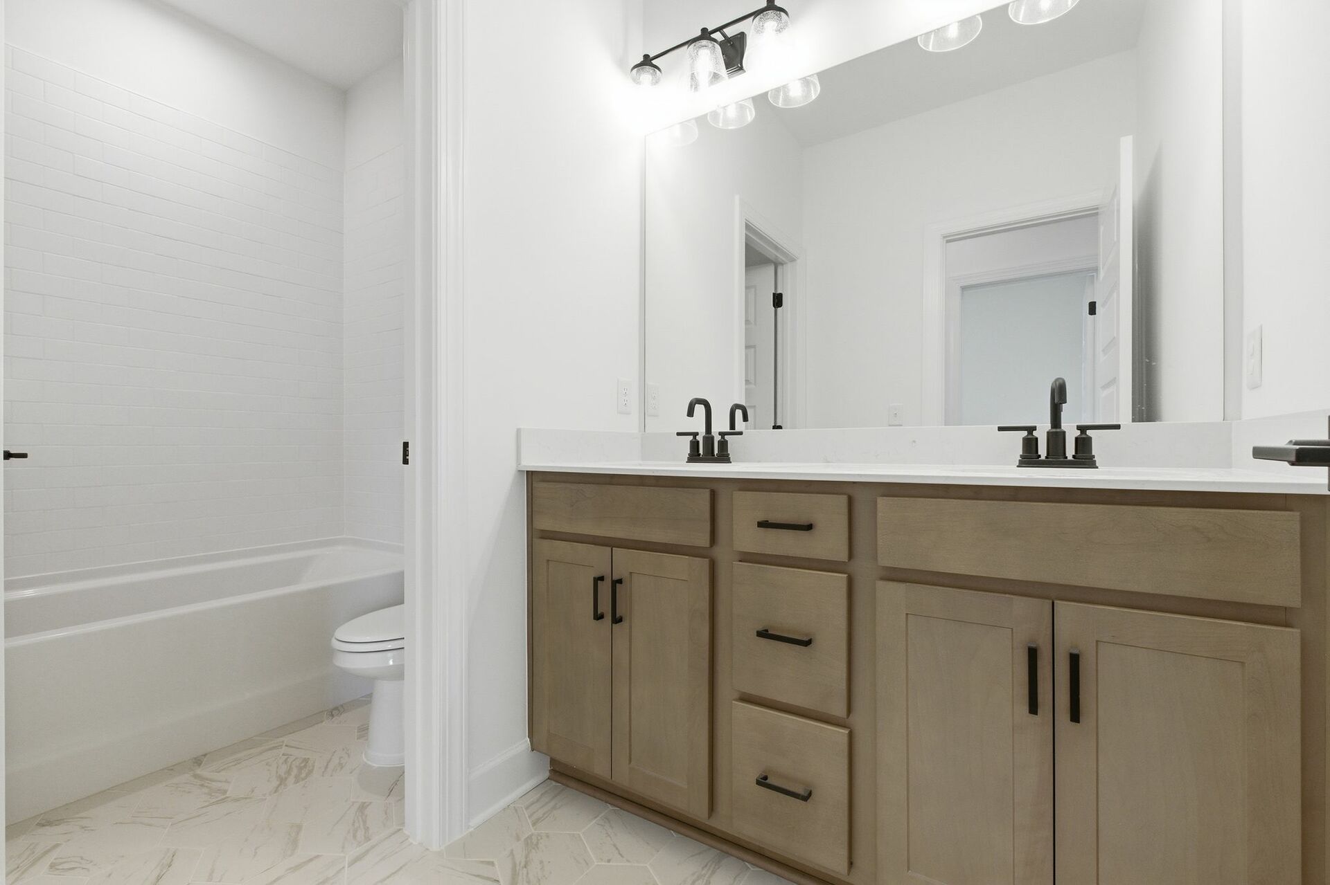 secondary bathroom with double sink vanity, wood cabinets, and a shower and tub combination