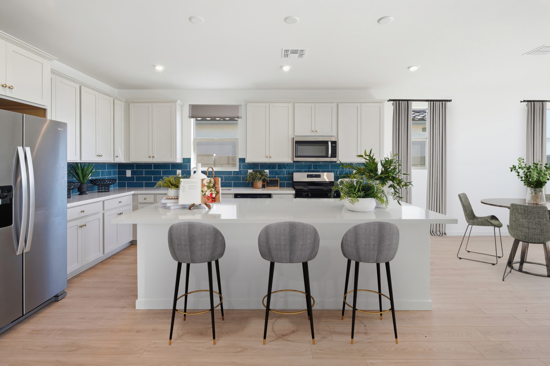 open-concept kitchen with grey barstools, white countertops, and stainless-steel appliances