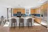 spacious kitchen with light brown cabinets, quartz countertops, and grey barstools