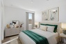 spacious bedroom with beige rug, large white bed with royal green duvet, and white nightstands