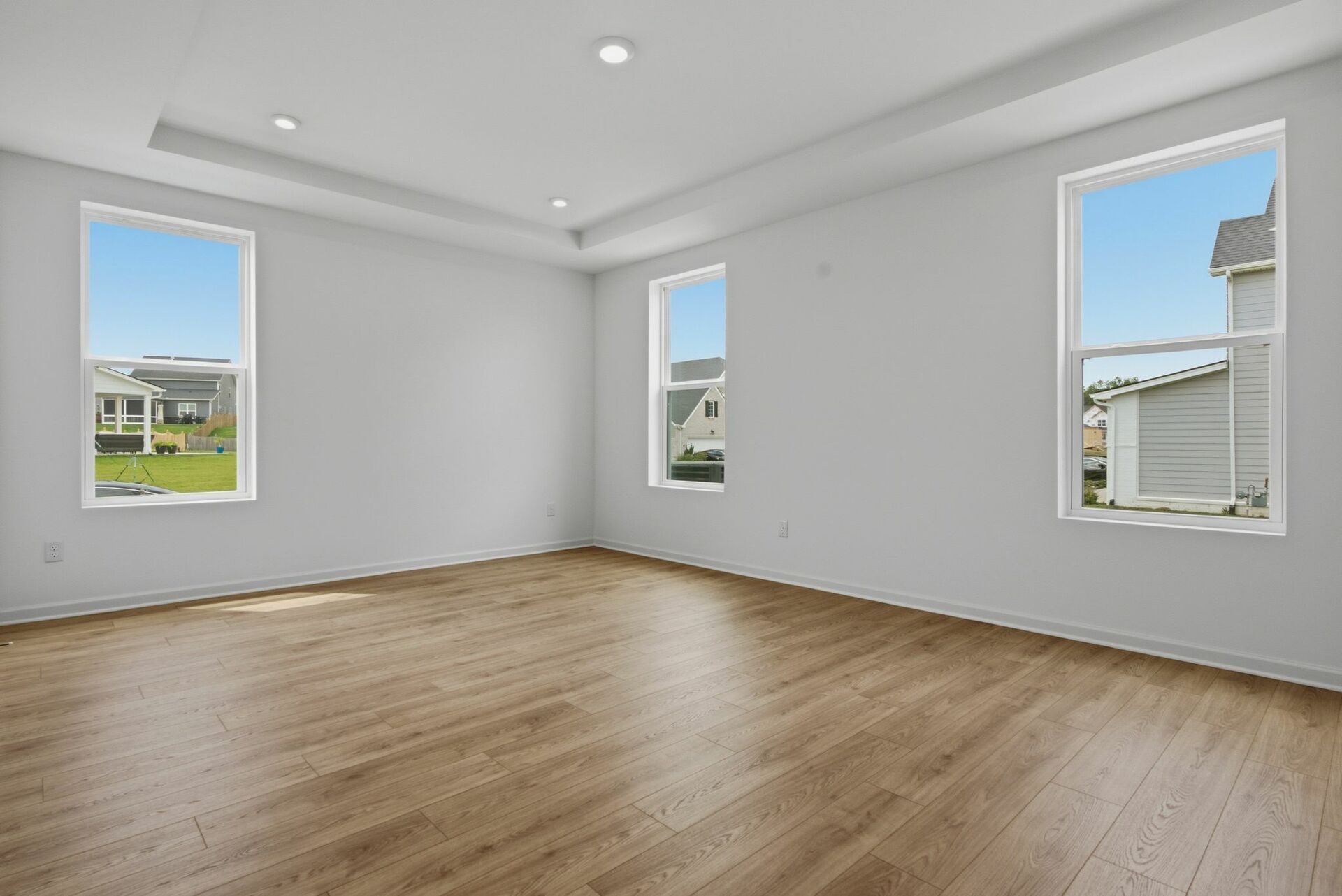 primary bedroom with wood floors, large windows, white walls, and tray ceiling