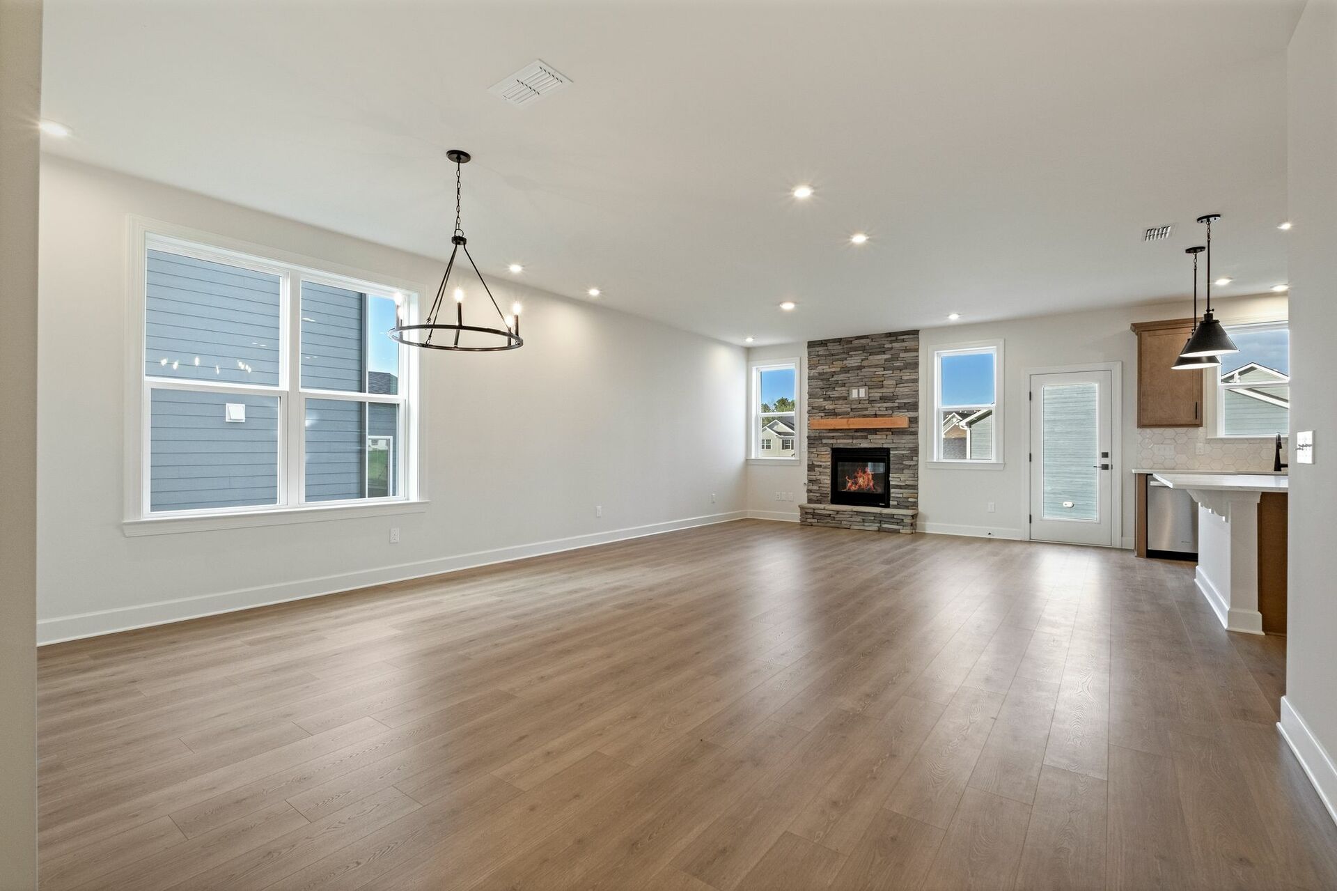 dining and great room with wood floors, black lighting fixtures, and a stone fireplace