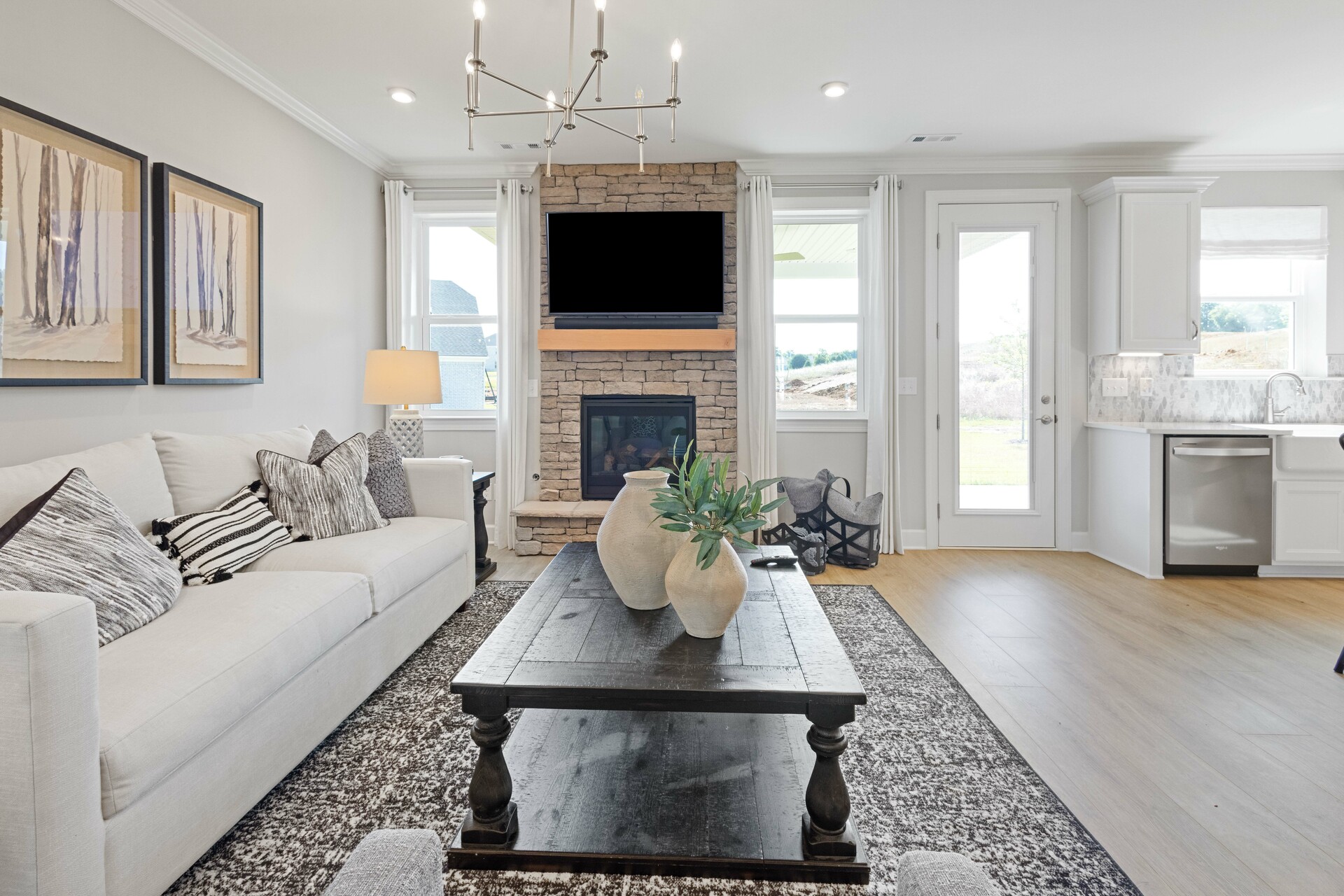 great room with wood flooring, white sofa, large area rug, stone fireplace, and large windows
