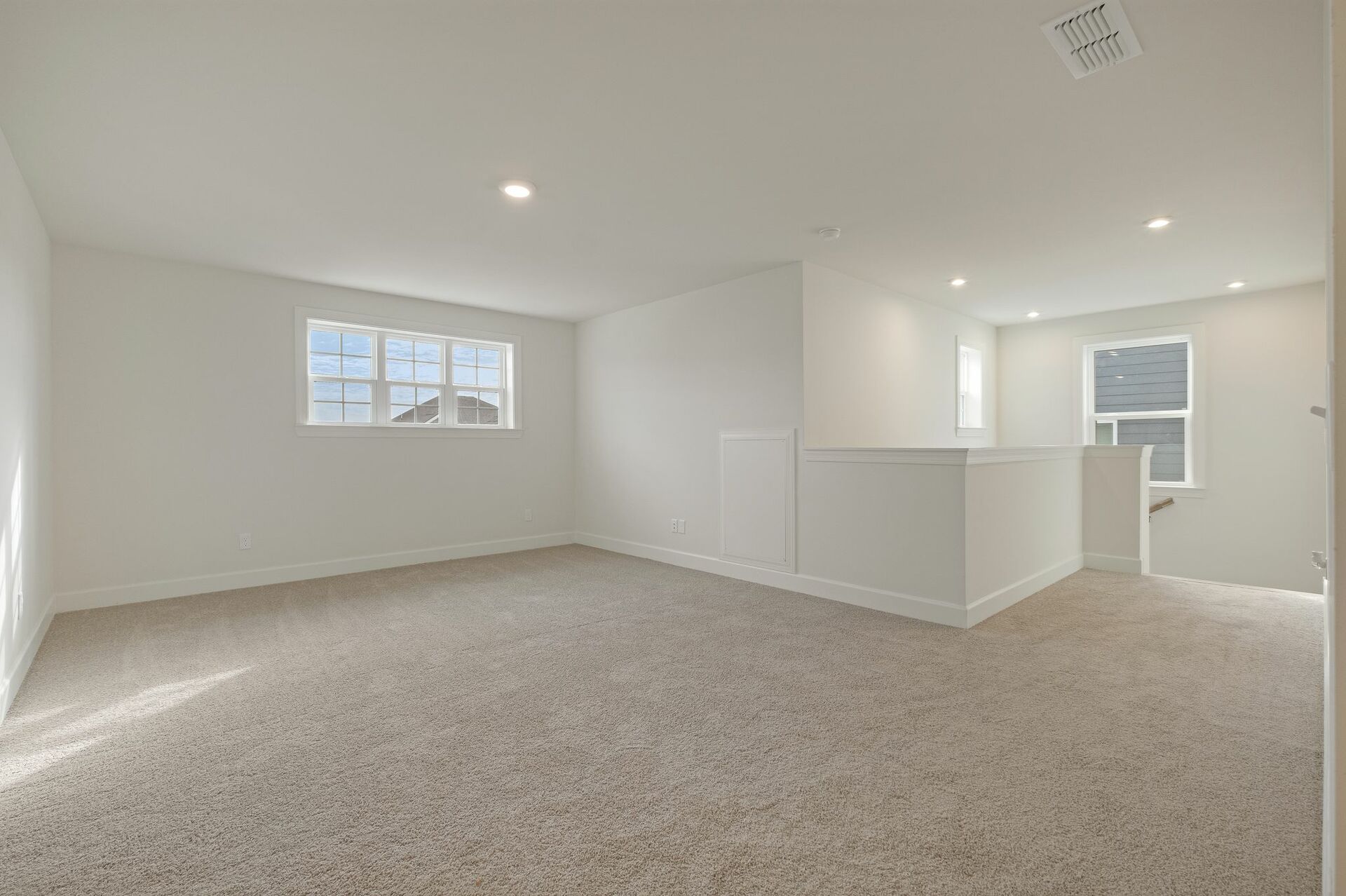 loft space with carpet flooring, large windows, and a view of the staircase