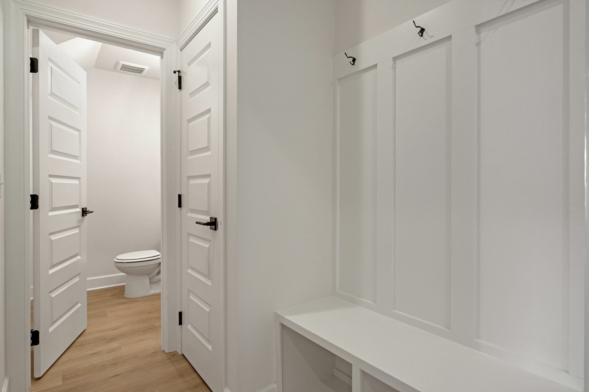 mudroom with valet bench with hooks and a view of the powder room