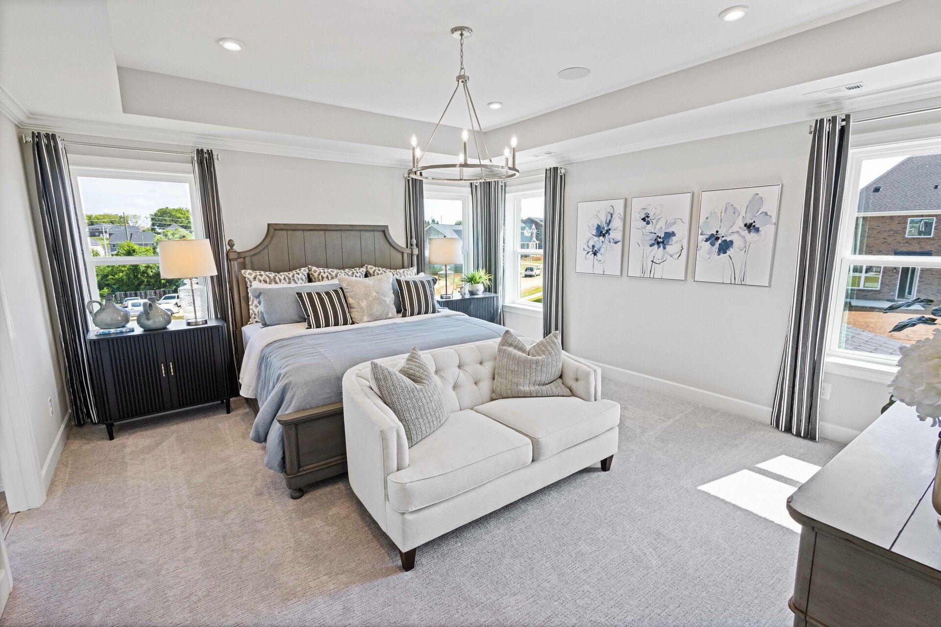 primary bedroom with carpet flooring, large bed, nightstands, large windows and a tray ceiling