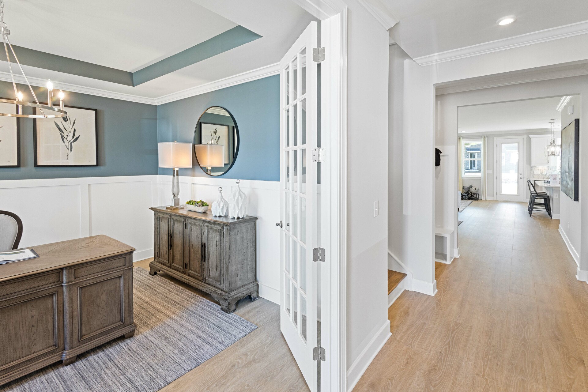 study with wood flooring, large desk and chair, judges paneling on the walls, and a tray ceiling