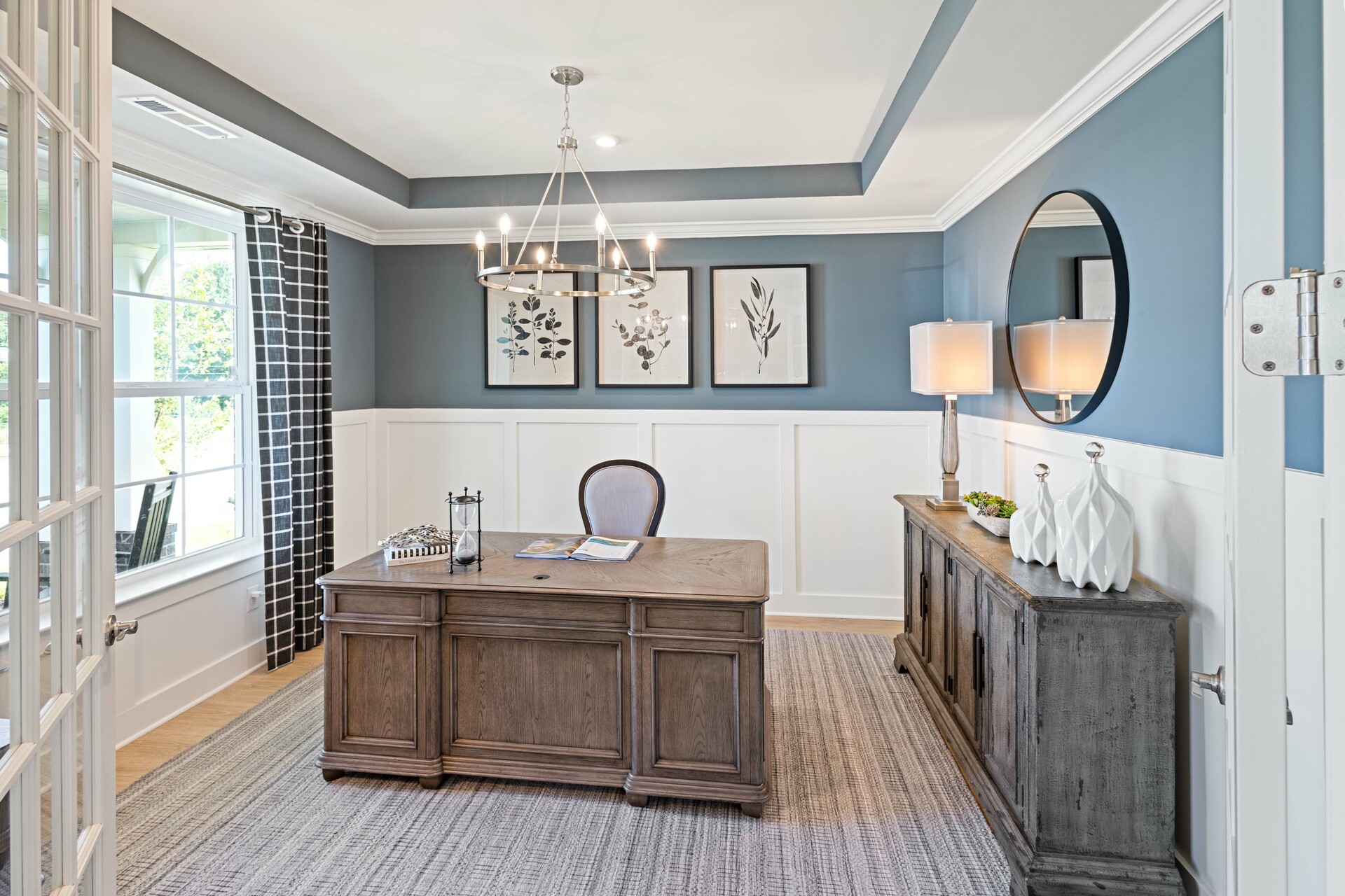 study with wood flooring, large desk and chair, judges paneling on the walls, and a tray ceiling
