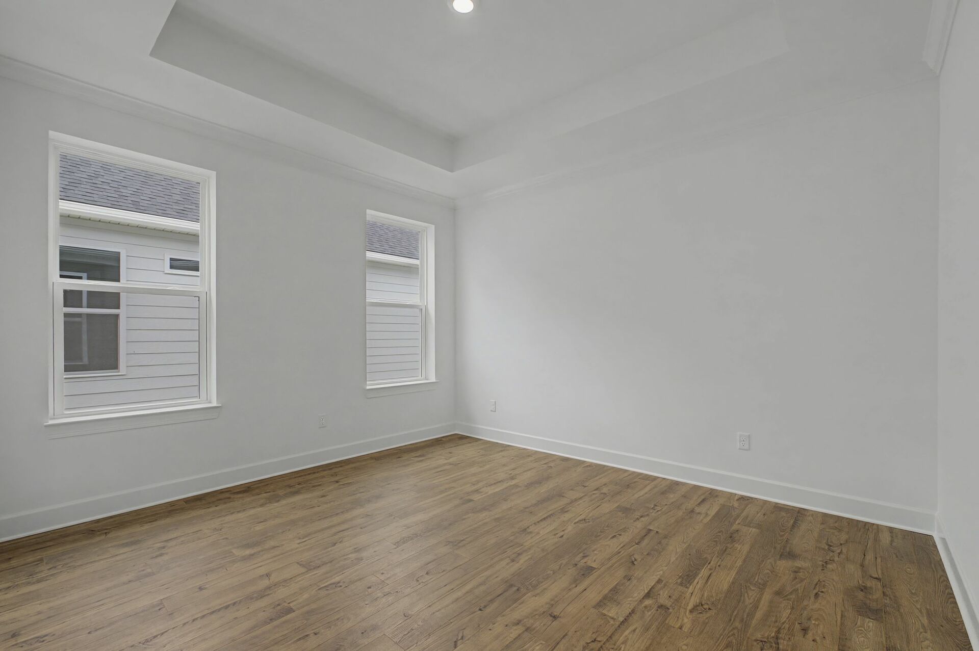 primary bedroom with wood flooring, large windows, and a tray ceiling