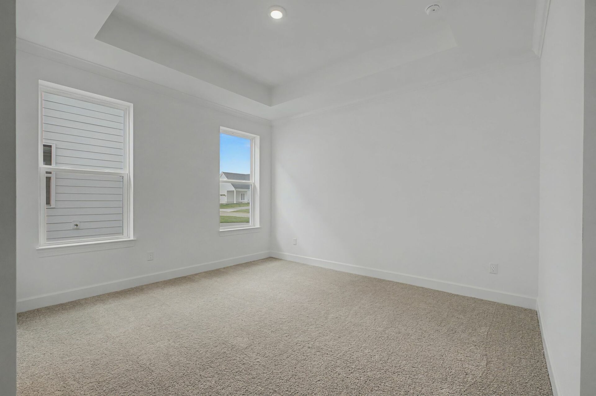 primary bedroom with wood flooring, large windows, and a tray ceiling