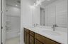secondary bathroom with double sink vanity, wood cabinets, and a shower and tub combination