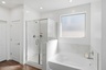 spacious bathroom with a walk-in shower, soaking tub and wood-like flooring 