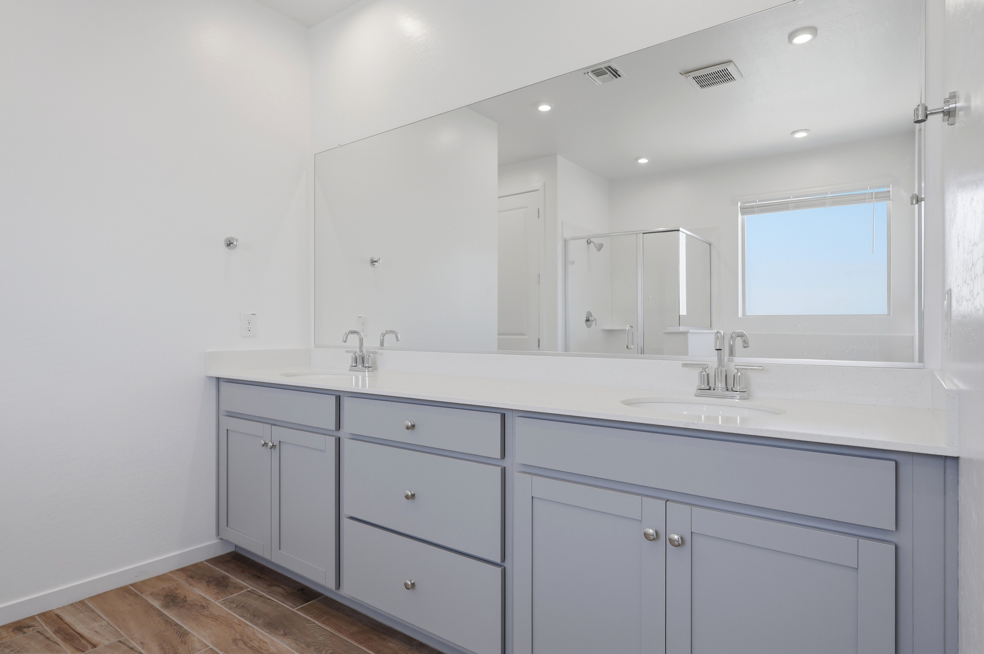 spacious bathroom with grey cabinets, chrome faucets, and a double sink