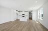 great room with hardwood floors and large windows attached to open concept kitchen with white cabinets and stainless steel appliances
