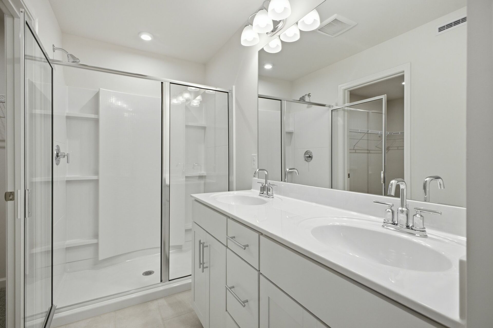 primary bathroom with oversized walk-in shower, dual sink vanity with white counter, white cabinets, and chrome hardware