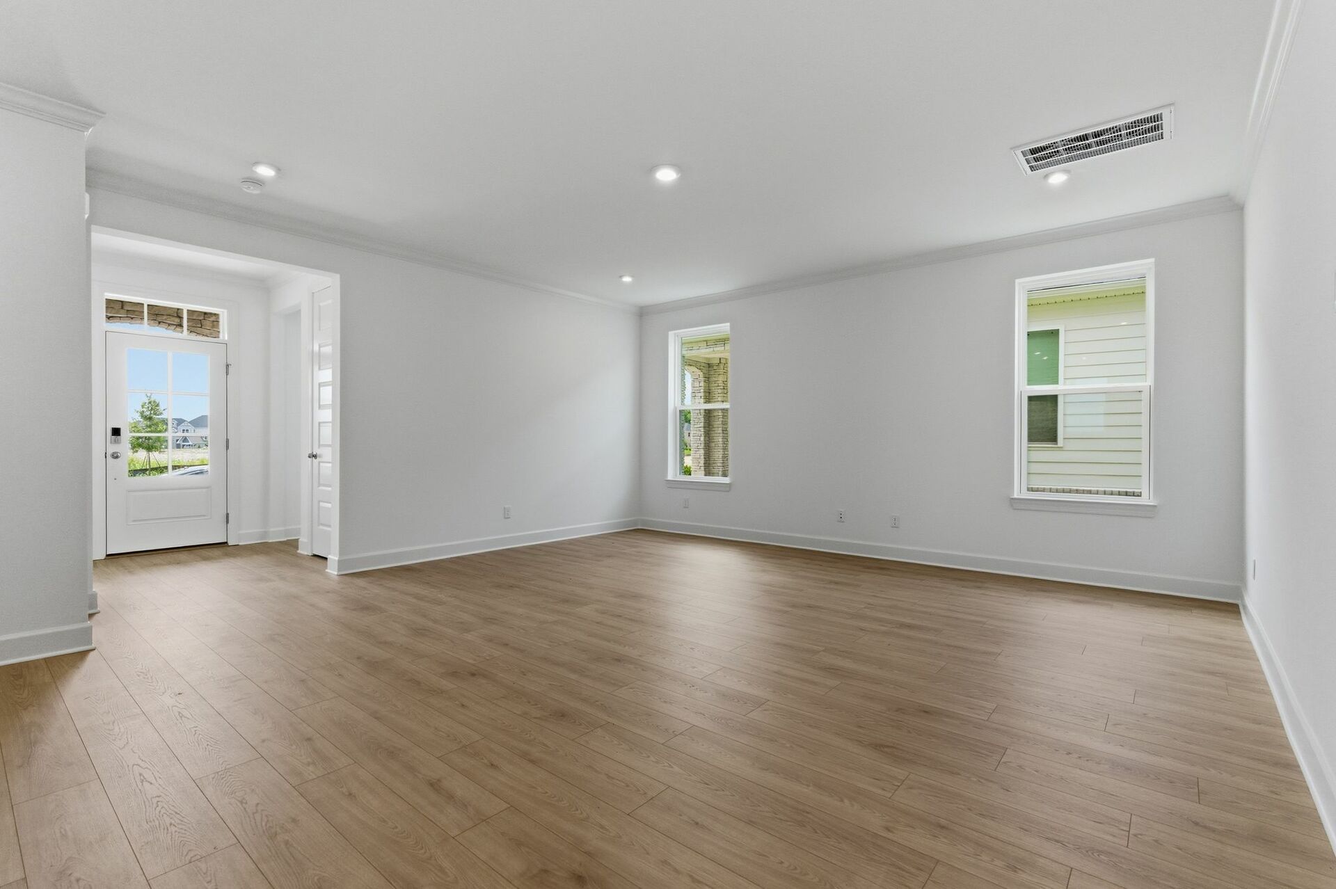 great room with light brown wood floors, large windows, white walls and white trim 