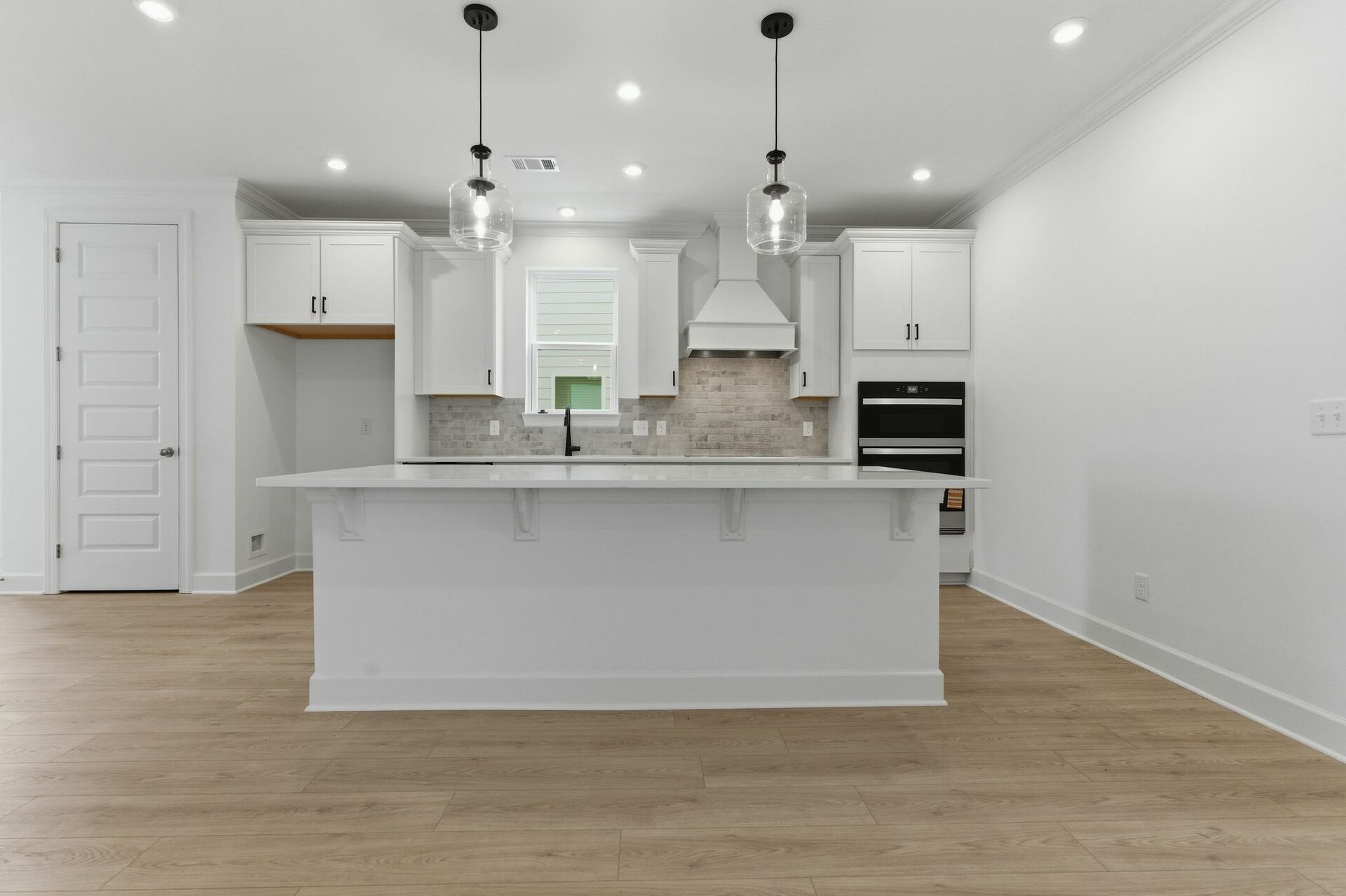 Kitchen with light brown wood floors, white cabinets, built in microwave oven combination, and white island with pendant lights