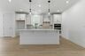 Kitchen with light brown wood floors, white cabinets, built in microwave oven combination, and white island with pendant lights