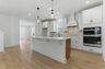 Kitchen with light brown wood floors, white cabinets, built in microwave oven combination, and white island with pendant lights