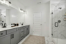 primary bathroom with double sink vanity, gray cabinets, a walk-in shower, and black fixtures