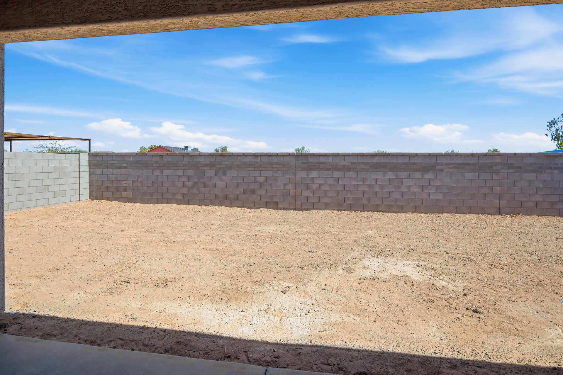 spacious dirt backyard with a concrete block wall 