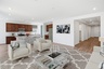 open-concept space with a large beige rug, a large white couch, and a glass coffee table.