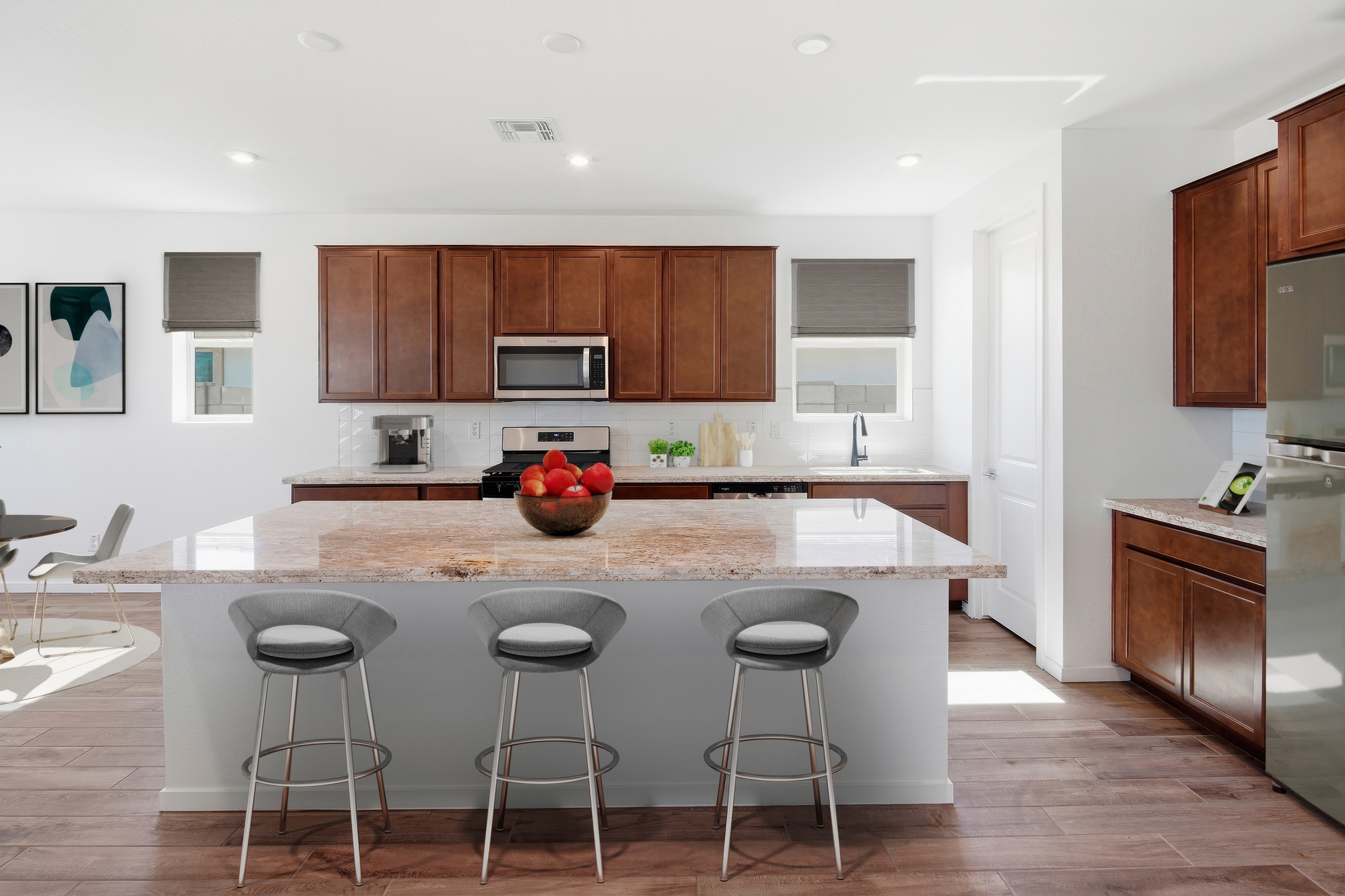 open-concept kitchen with grey barstools, brown cabinets, and bianco lucre quartz countertops