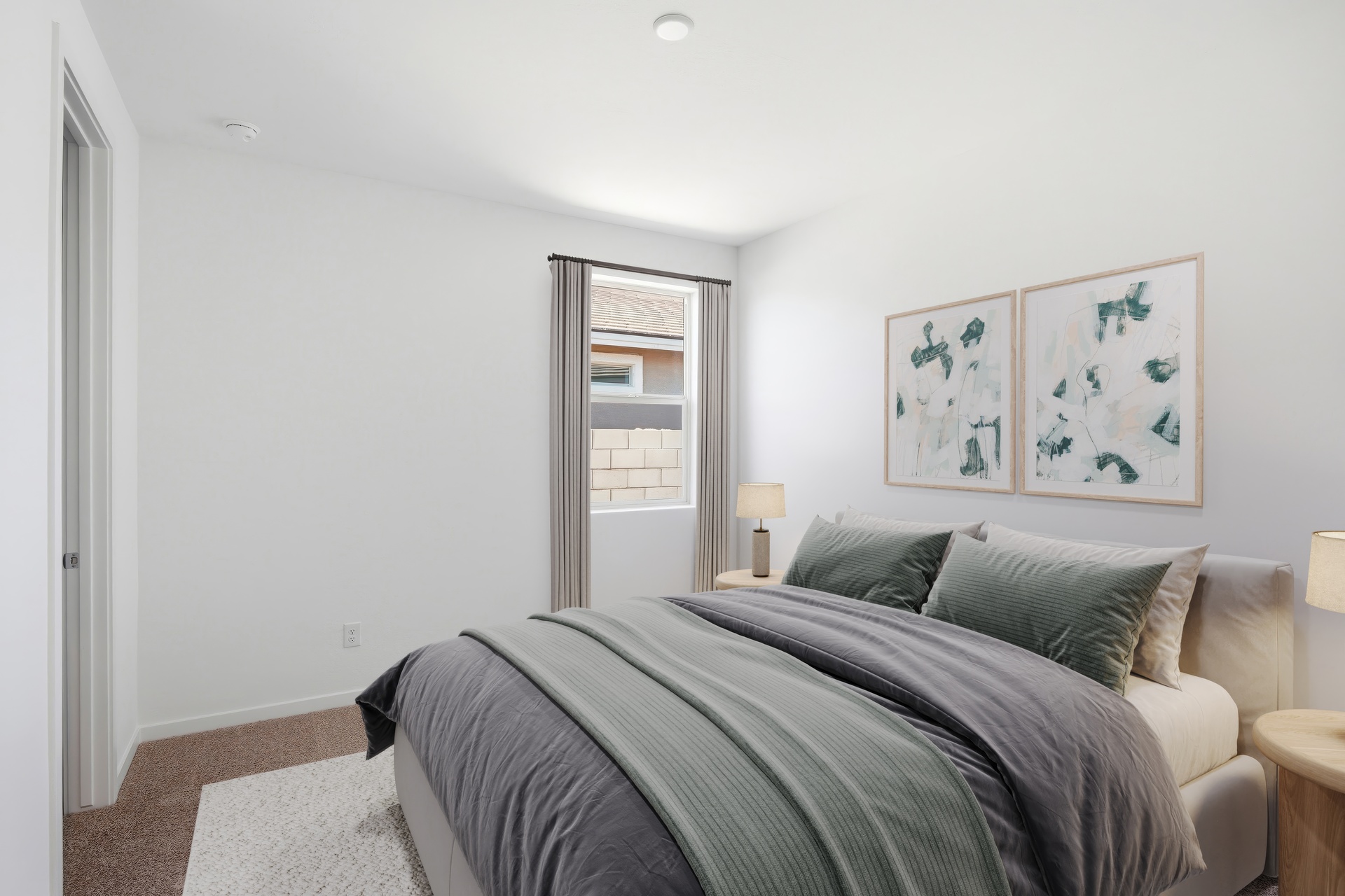 large bed with grey comforter, white rug, and oak nightstands