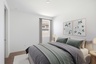 large bed with grey comforter, white rug, and oak nightstands
