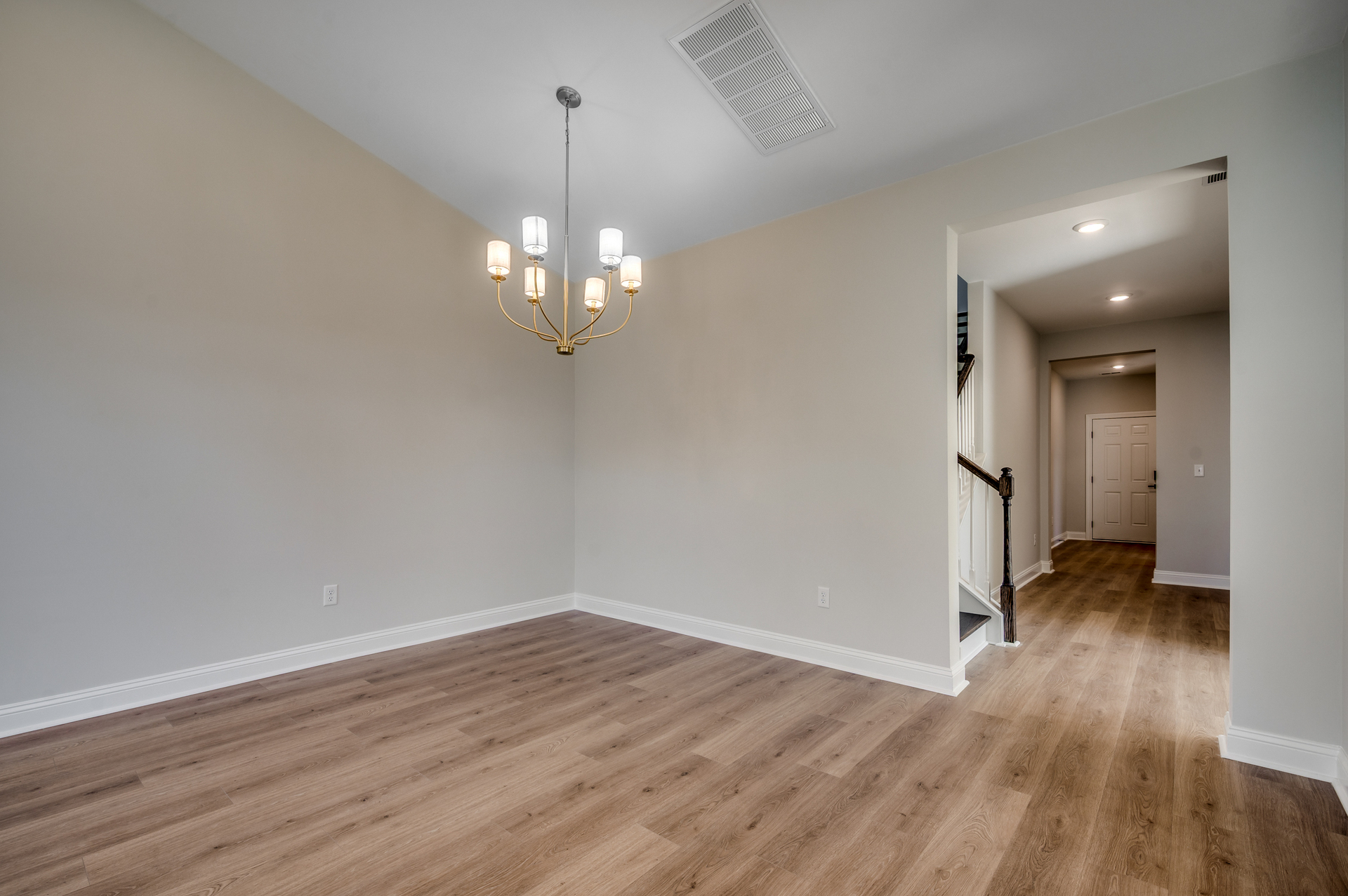 spacious room with tan walls, hardwood flooring and gold chandelier 