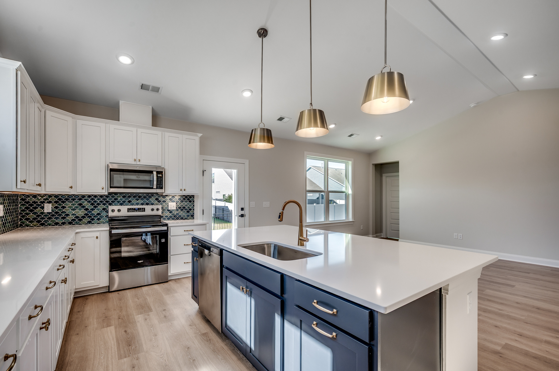 dark blue island cabinets with large sink in island, white quartz countertops and stainless-steel appliances 