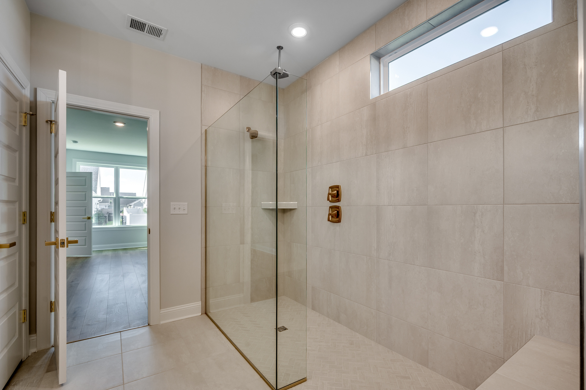 spacious spa-inspired walk-in shower with gold hardware, tiled flooring and tiled walls