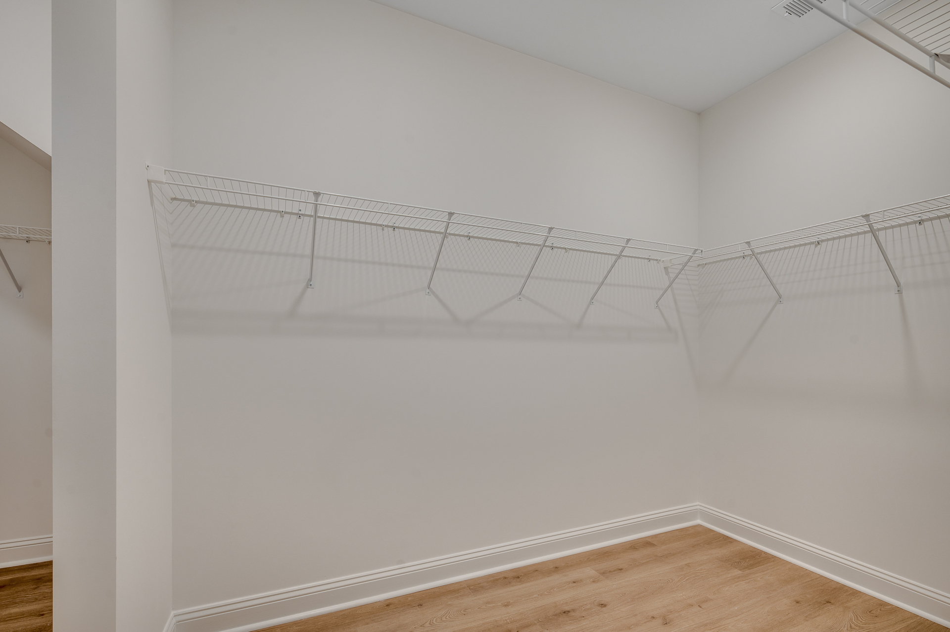 spacious walk-in closet with light gray walls and white wire built in shelving 